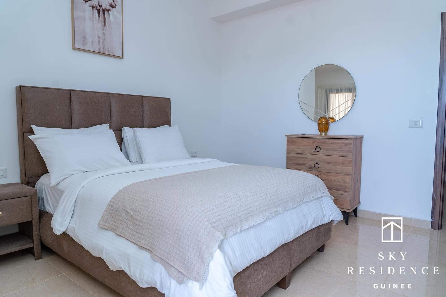 Chambre lumineuse Sky Residence avec commode et miroir rond